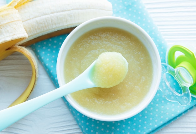 Bowl with baby food and banana on table