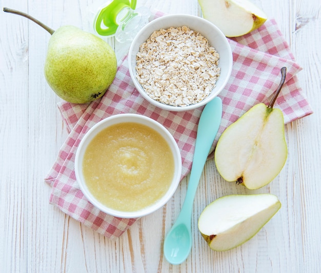 Bowl with baby food and pears on table