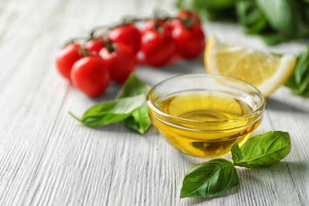 Bowl with basil oil green leaves and tomatoes on wooden table