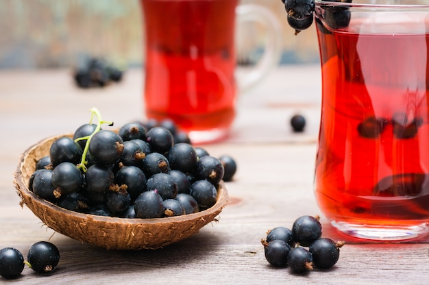 Bowl with black currant berries and fresh compote of ripe black currant in a glass on a wooden table