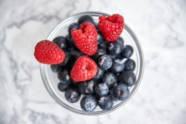 Bowl with blueberries and fresh raspberries on a marble background