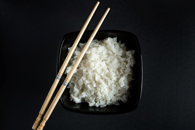 Ciotola con riso bollito su sfondo nero. cibo asiatico e bacchette di bambù.