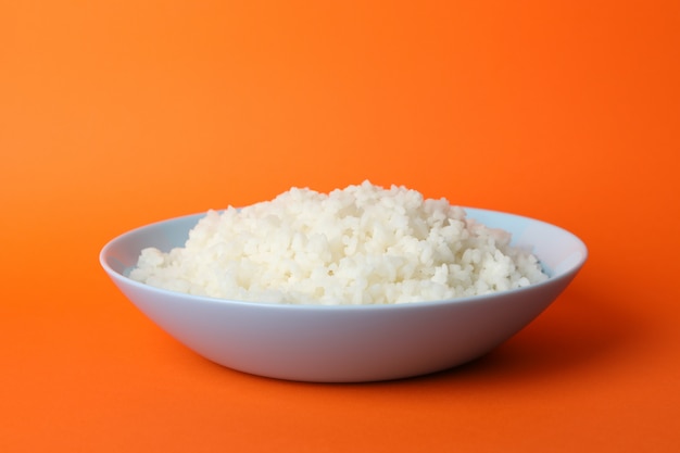 Bowl with boiled rice on orange surface