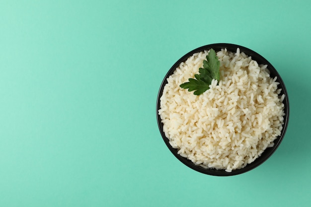 Bowl with boiled rice and parsley on mint surface