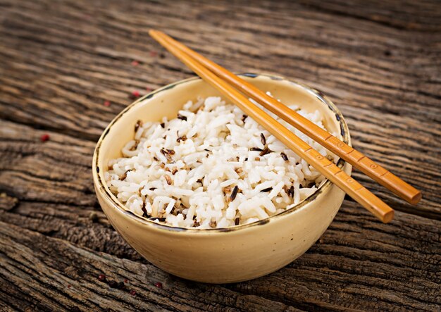 Bowl with boiled rice on a wooden table.