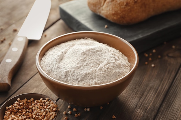 Bowl with buckwheat flour on wooden table