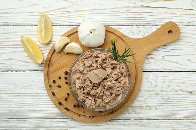 Bowl with canned tuna on white wooden background