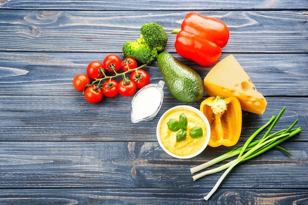 Bowl with cheese sauce and different products on wooden background