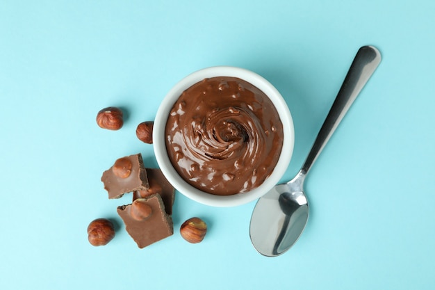 Bowl with chocolate paste, nuts, chocolate and spoon on blue background