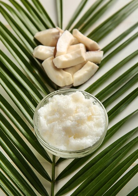 Bowl with coconut body scrub and palm leaf on white background