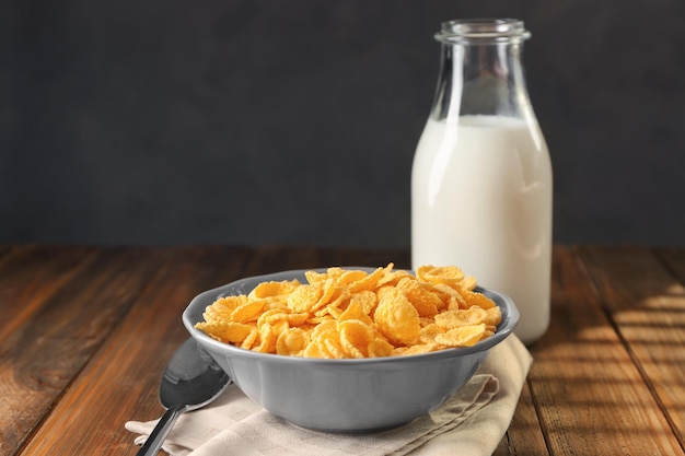 Bowl with corn flakes and bottle of milk on wooden table