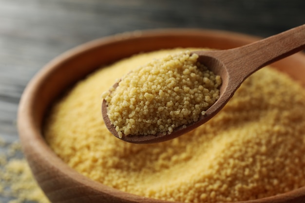 Bowl with couscous and spoon on wooden background