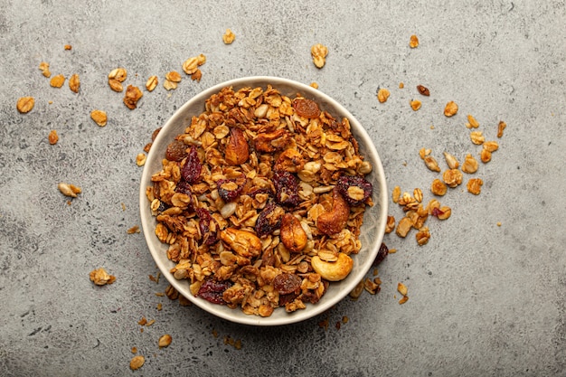 Bowl with crispy homemade granola, healthy breakfast cereal granola with oatmeal, seeds, nuts, berries on rustic stone background from above