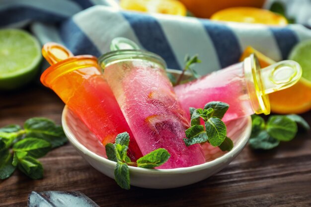 Bowl with delicious citrus popsicles and fresh fruits on wooden table