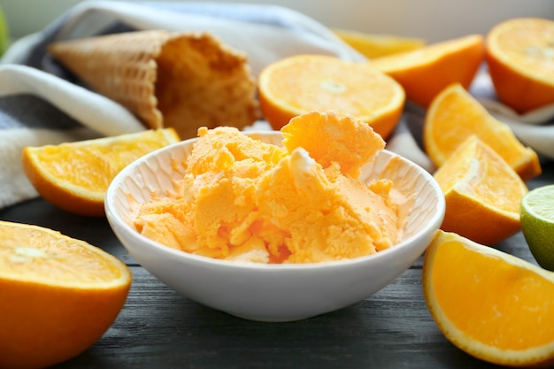 Bowl with delicious ice-cream and oranges on wooden table