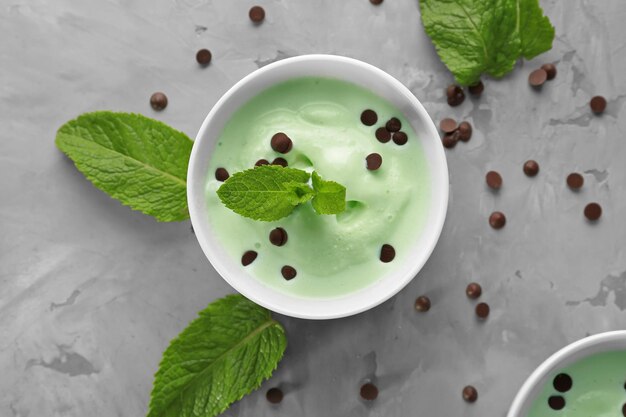 Bowl with delicious mint chocolate chip ice cream and fresh leaves on grey table