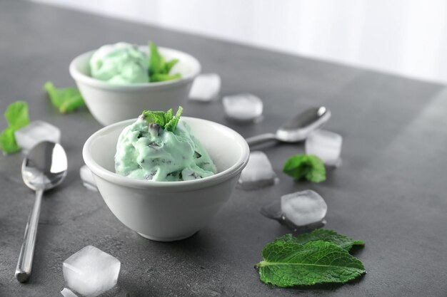 Foto ciotola con delizioso gelato alla menta con scaglie di cioccolato e cubetti di ghiaccio sul tavolo grigio