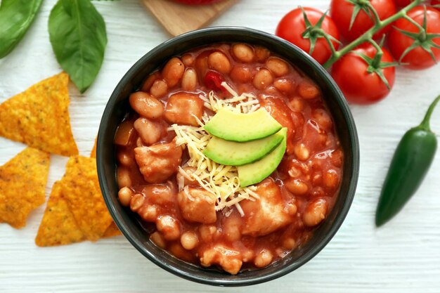 Bowl with delicious turkey chili on wooden background