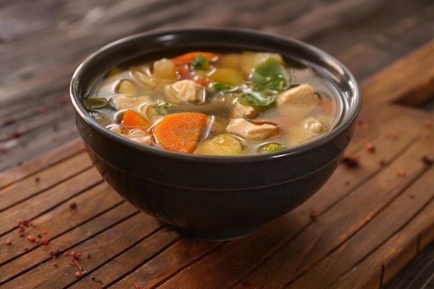 Bowl with delicious turkey soup on wooden board