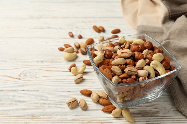 Bowl with different nuts on white wooden background