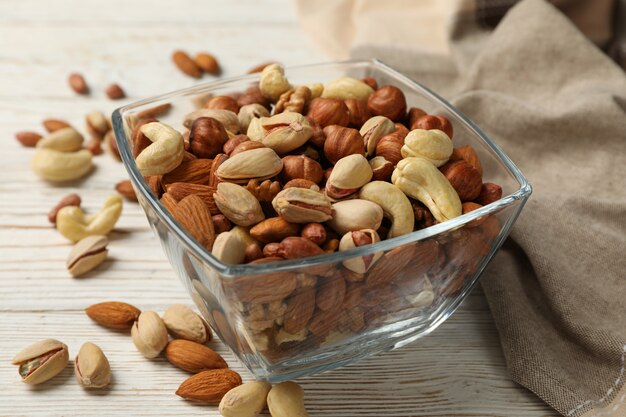 Bowl with different nuts on white wooden background