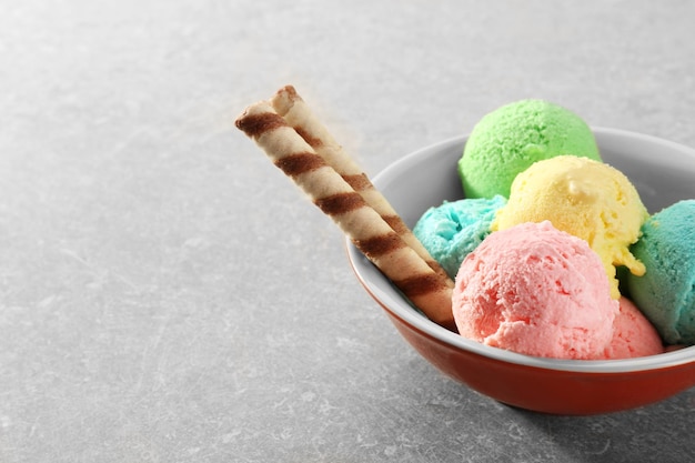 Bowl with different tasty ice cream and wafer sticks on gray background