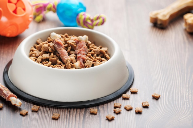 A bowl with dog food dog treats and toys on a wooden floor concept of healthy food for dogs