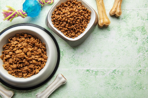 A bowl with dog food dog treats and toys on a wooden floor