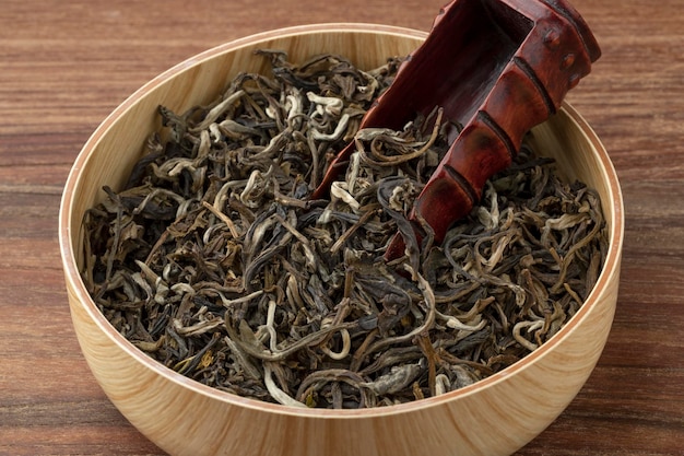 Bowl with dried Chinese Monkey King of Jasmin tea leaves and a bamboo scoop close up