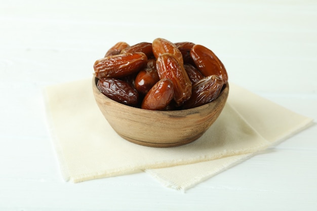 Bowl with dried dates on kitchen napkin on white wooden table