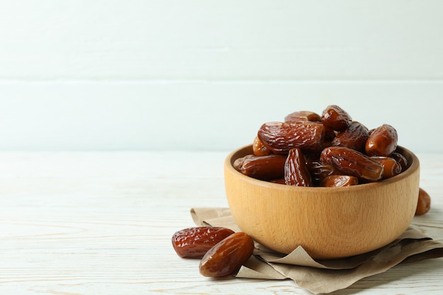 Bowl with dried dates on paper on white wooden table