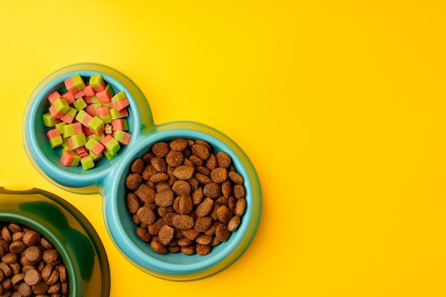 Bowl with dry pet food on yellow background studio shot