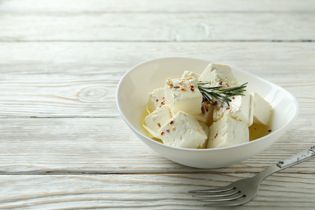 Bowl with feta cheese and fork on white wooden surface