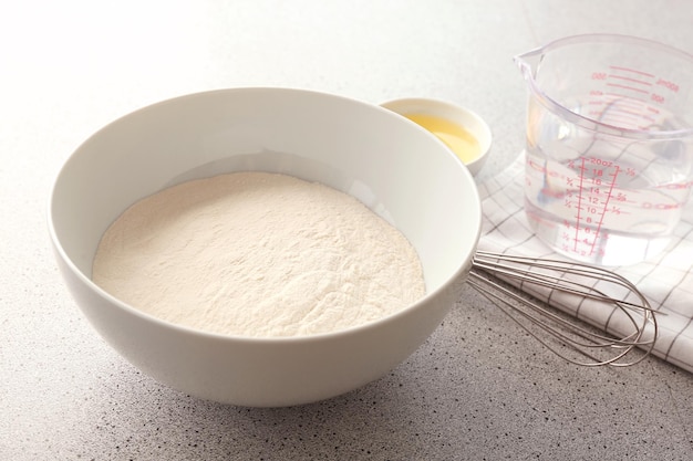 Bowl with flour and ingredients for dough on table