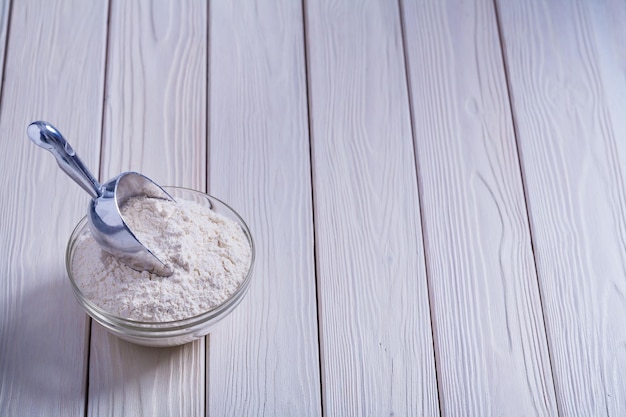 Bowl with flour and scoop on white painted old wooden board food and drink concept