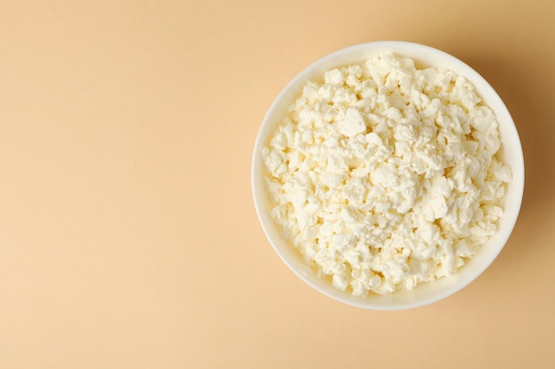 Bowl with fresh cottage cheese on beige background