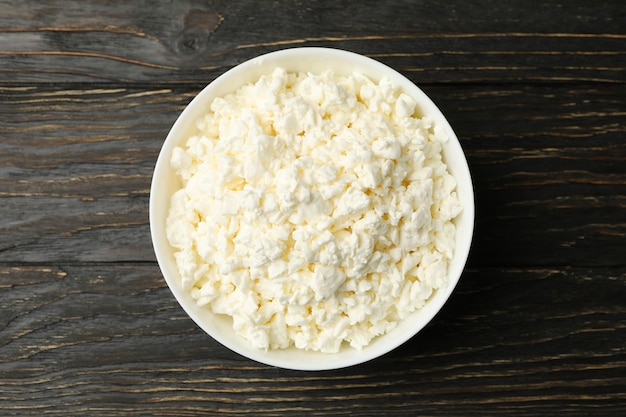 Bowl with fresh cottage cheese on wooden background