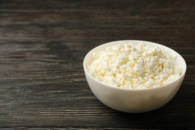 Bowl with fresh cottage cheese on wooden background
