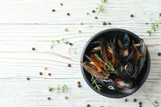 Bowl with fresh mussels on white wooden table