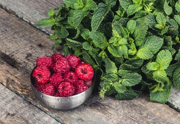 Photo bowl with fresh ripe raspberries on a wooden table and mint