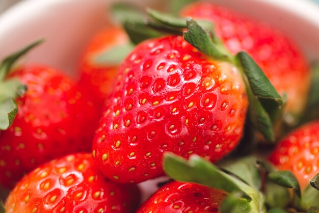 Bowl with fresh strawberry on blue wooden table.