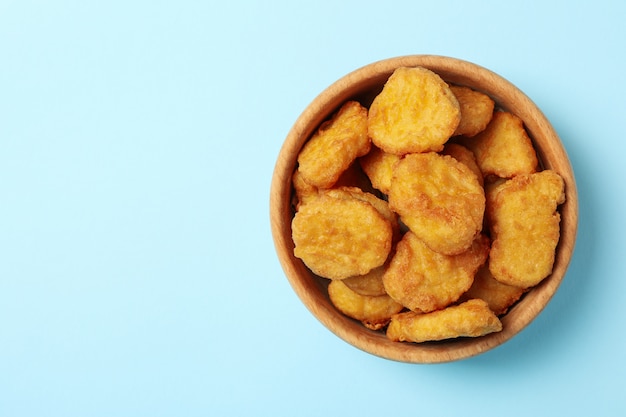 Bowl with fried chicken nuggets on blue background