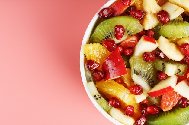 Bowl with fruit salad on a pink background. Juicy and ripe fruit slices. Top view