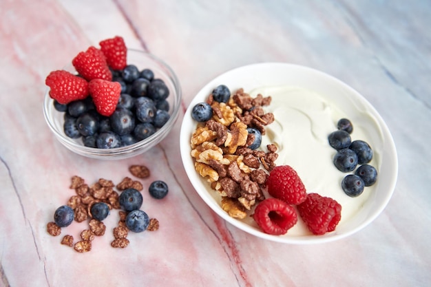 Bowl with Greek yogurt nuts cereals blueberries and fresh raspberries on a marble background