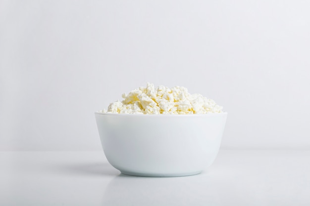 白い背景の上の自家製カッテージチーズをボウルします。カルシウムと健康的な乳製品の概念。栄養の概念