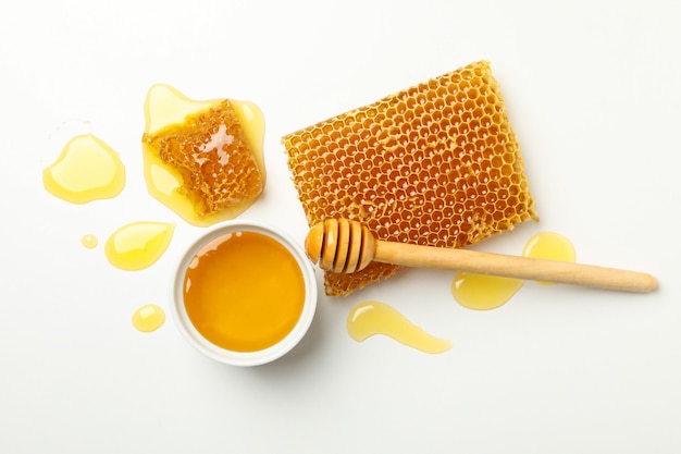 Bowl with honey, dipper and honeycombs on white background