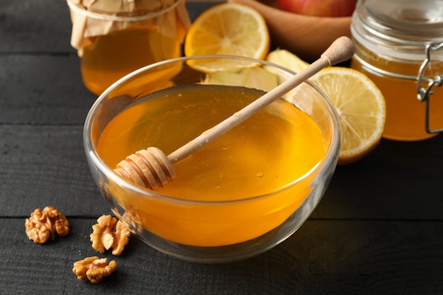 Bowl with honey, dipper and walnut on wooden background