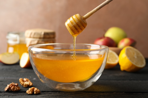 Bowl with honey, dipper and walnut on wooden background