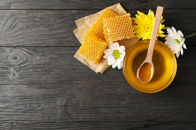 Bowl with honey, honeycombs and flowers on wooden background