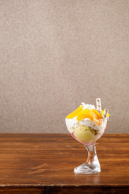 Bowl with ice cream and fruits on wooden table over empty wall Copy space